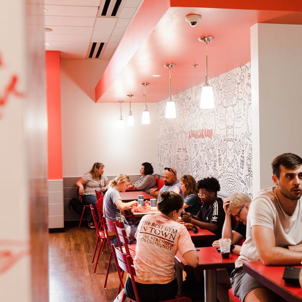 Diners enjoying meals at red tables in Nashville Coop, with a doodle-covered wall and modern lighting.