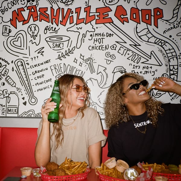 Two women enjoying fried chicken and fries at Nashville Coop, with a doodle-covered wall behind them.