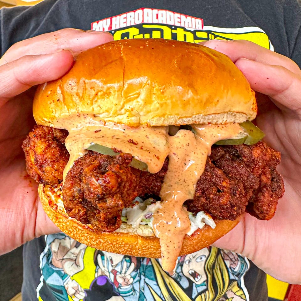 Hands holding a Nashville Coop fried chicken sandwich with sauce dripping down.