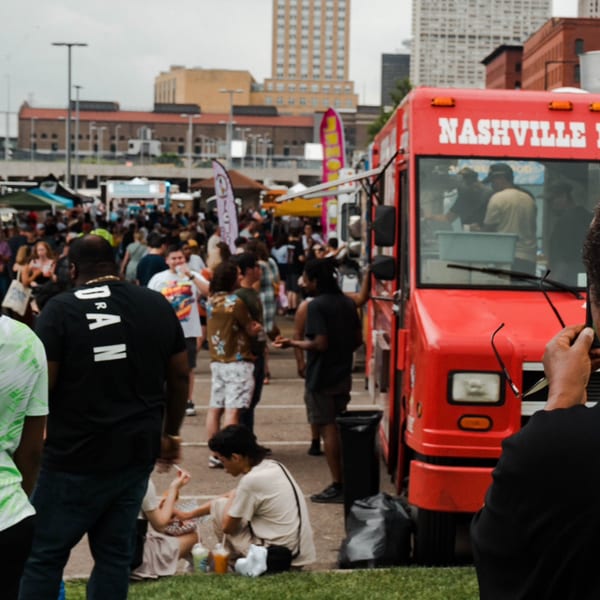 A Nashville Coop food truck at an outdoor festival with many people milling around.