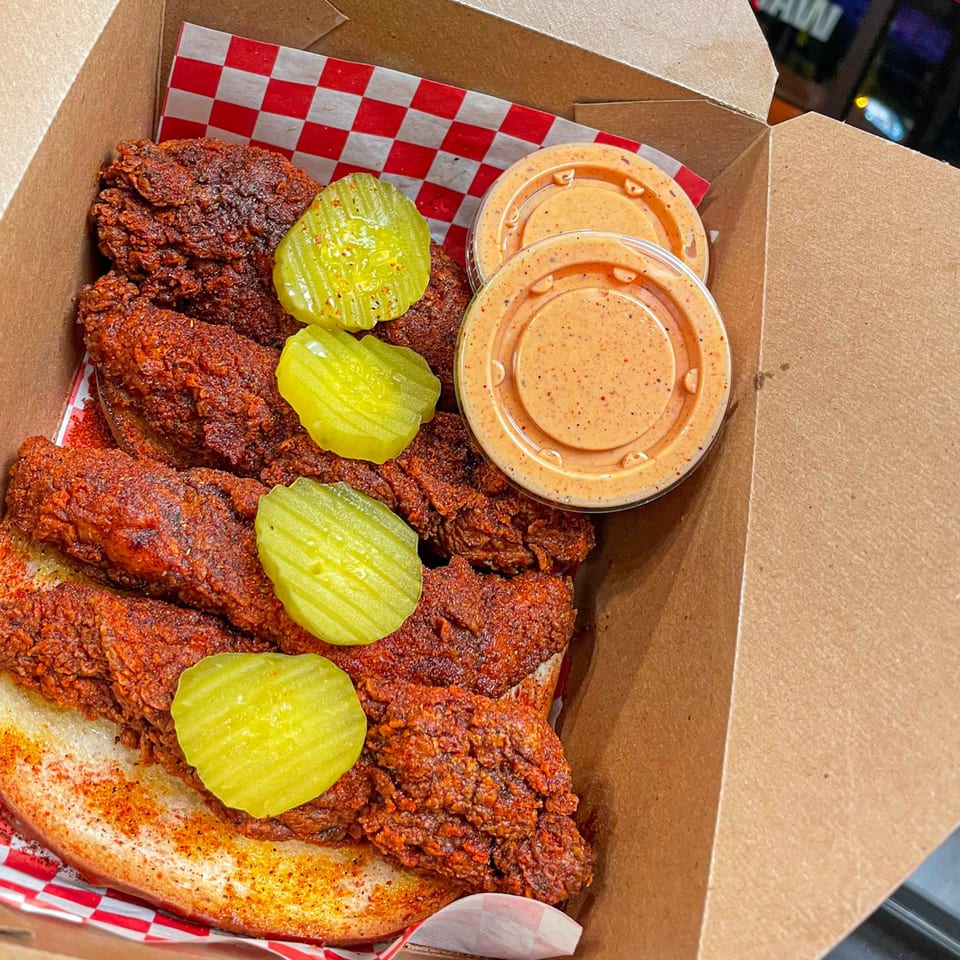 Nashville Coop's fried chicken tenders with pickles and dipping sauce in a takeout box.