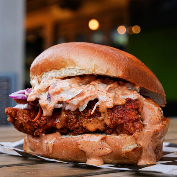 Nashville Coop's fried chicken sandwich with coleslaw and spicy sauce on a bun.