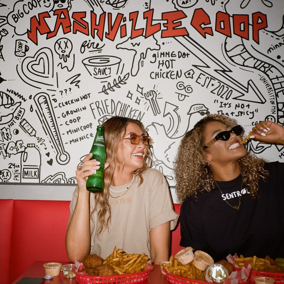 Two women enjoying Nashville Coop fried chicken and fries at a red booth with a doodle wall.