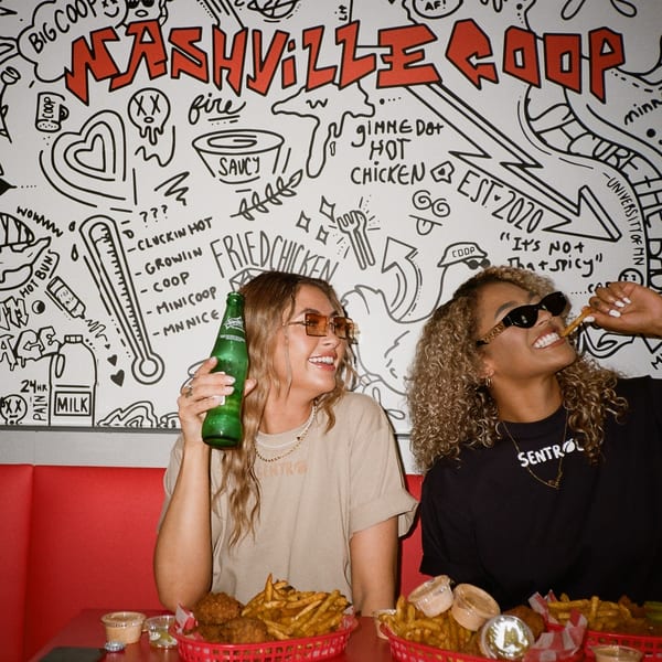 Two women enjoying Nashville Coop fried chicken and fries in a booth with a doodle-covered wall.