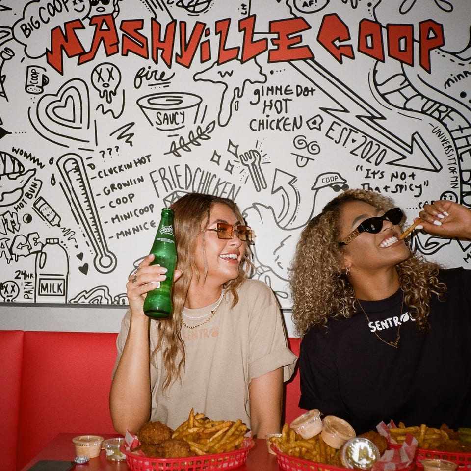 Two women enjoying Nashville Coop fried chicken and fries in a booth with a doodle-covered wall.